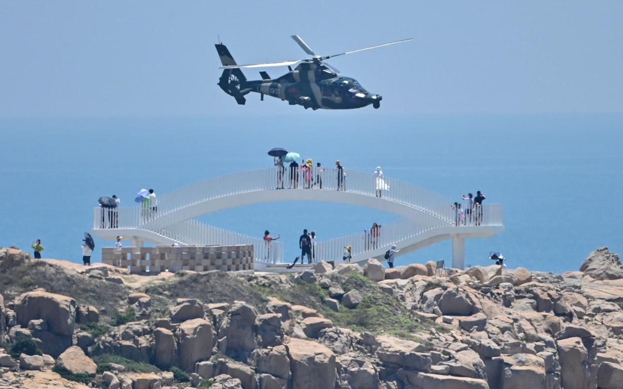 Tourists look on as a Chinese military helicopter flies past Pingtan island, one of mainland China's closest point from Taiwan - HECTOR RETAMAL /AFP