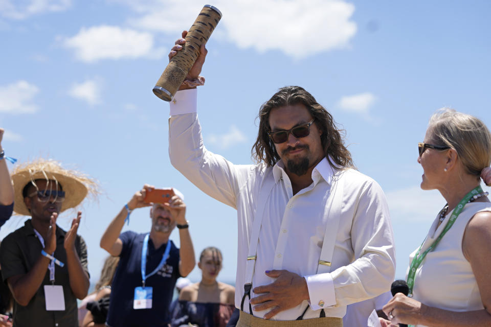 Actor Jason Momoa holds the "Nature Batton" after arriving to meet participants at the United Nations' Youth and Innovation Forum at Carcavelos beach, outside Lisbon, Sunday, June 26, 2022. From June 27 to July 1, the United Nations is holding its Oceans Conference in Lisbon expecting to bring fresh momentum for efforts to find an international agreement on protecting the world's oceans. (AP Photo/Armando Franca)