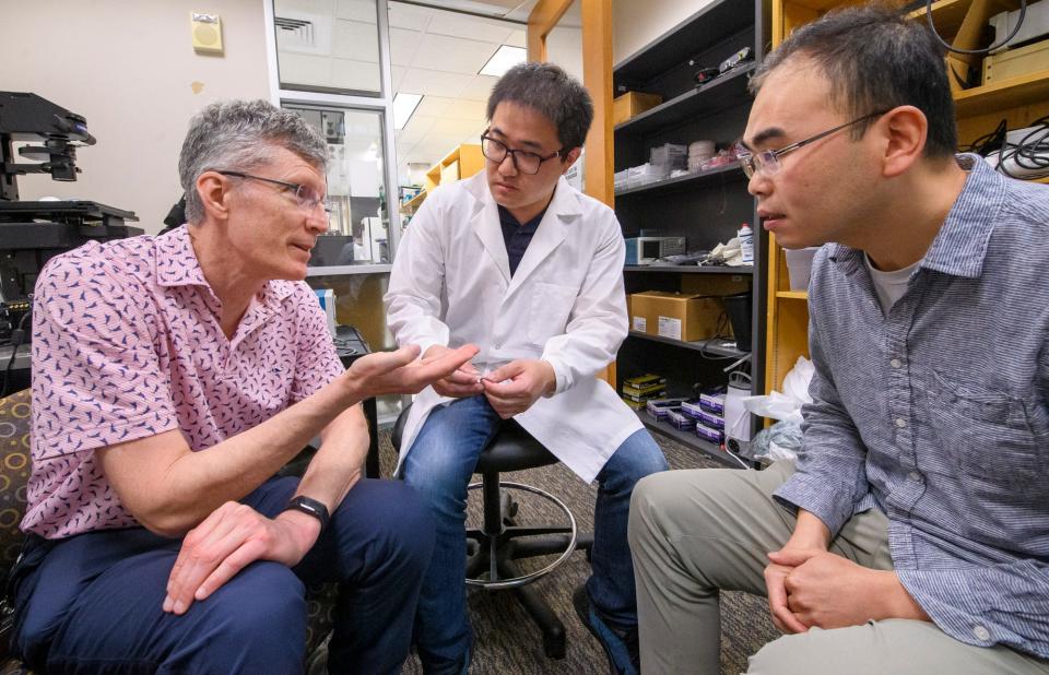 Ken Mackie, left, Xiang Li, middle, and Feng Guo discuss their opioid overdose detection device while working at Indiana University on Thursday, May 19, 2022.