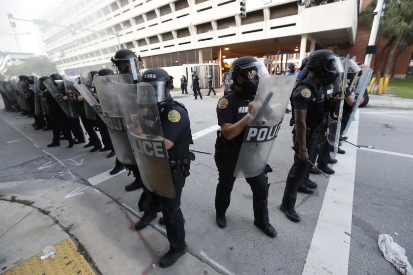 Police officers stand in formation against protesters throwing rocks and waterbottles during a demonstration next to the city of Miami Police Department, Saturday, May 30, 2020, downtown in Miami. Protests were held throughout the country over the death of George Floyd, a black man who died after being restrained by Minneapolis police officers on May 25. (AP Photo/Wilfredo Lee)