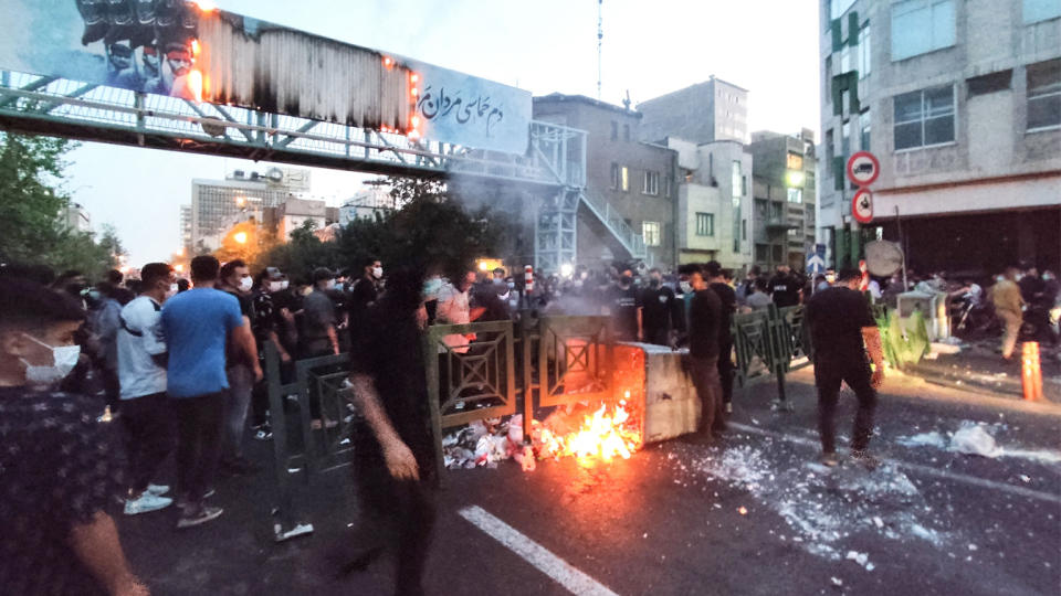 Iranian demonstrators gather around a blaze in the middle of a wide thoroughfare.