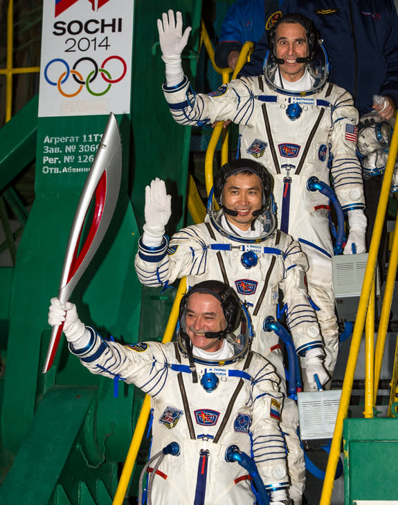 Russian cosmonaut Mikhail Tyurin, Expedition 38 Soyuz commander, holds the Olympic torch as Flight Engineer Koichi Wakata of Japan and Rick Mastracchio of NASA (top) wave farewell prior to boarding the Soyuz TMA-11M rocket for launch, Thursday,