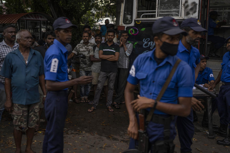 Police officers stand guard as people wait in queue to buy petrol at a fuel station, in Colombo, Sri Lanka, July 17, 2022. Bankruptcy has forced the island nation's government to a near standstill. Parliament is expected to elect a new leader Wednesday, paving the way for a fresh government, but it is unclear if that's enough to fix a shattered economy and placate a furious nation of 22 million that has grown disillusioned with politicians of all stripes. (AP Photo/Rafiq Maqbool)