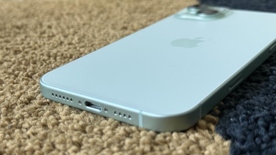 iPhone 15 Plus screen down on a rug showing the USB-C port on the bottom