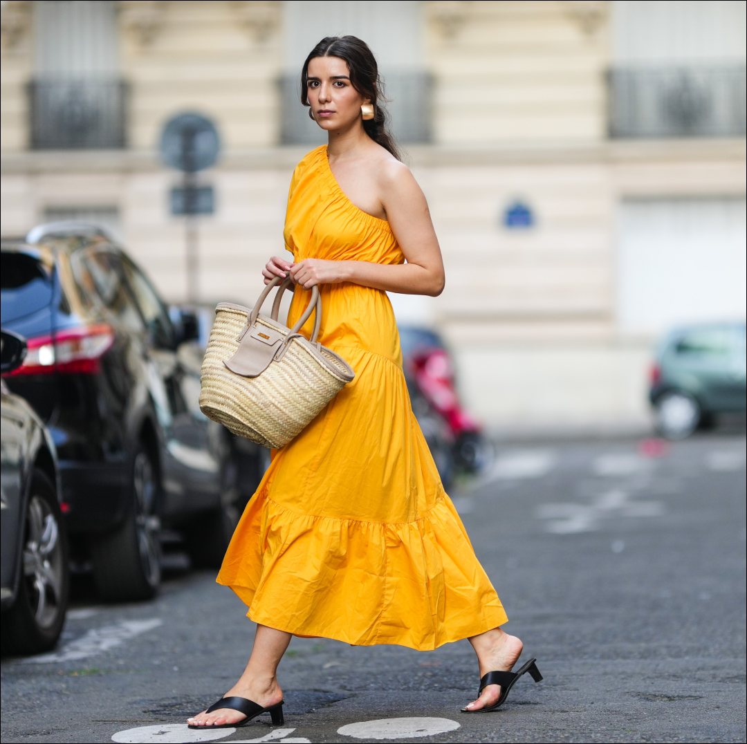  Ketevan Giorgadze @katie.one wears a one shoulder cut out maxi dress in orange from Mango, oversized golden hoop earrings from Zara, flip flop heeled black sandals shoes from APC Paris, a Le Grand Panier beach straw bag by Jacquemus, on August 12, 2021 in Paris, France. (Photo by Edward Berthelot/Getty Images). 