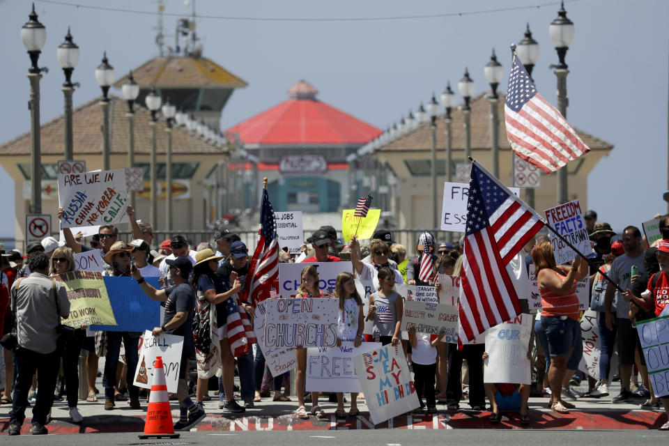 Protesters hold signs and wave flags during a May Day demonstration at the pier Friday, May 1, 2020, in Huntington Beach, Calif., during the coronavirus outbreak. (AP Photo/Chris Carlson)