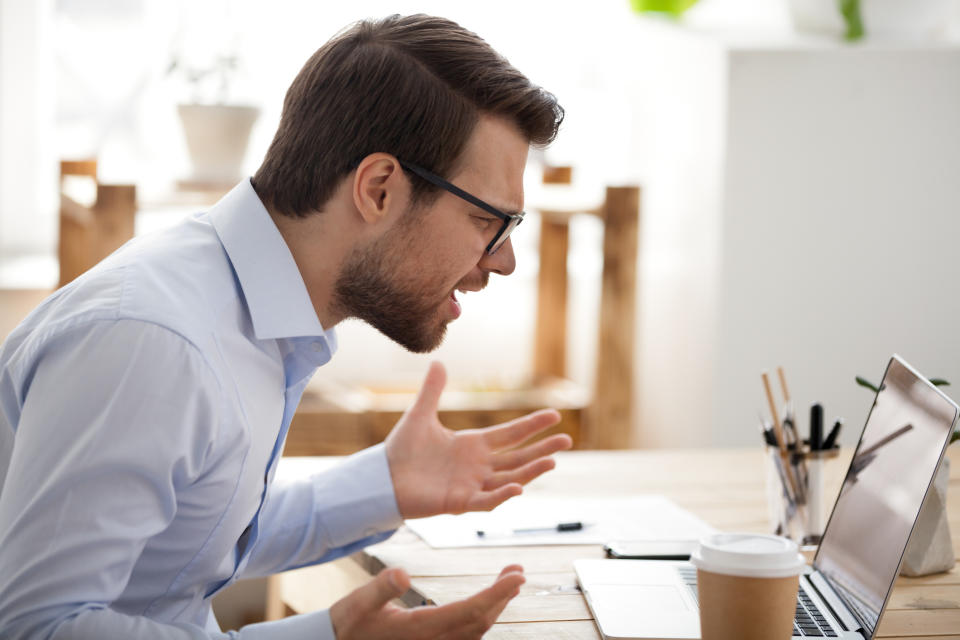 Man looking at laptop computer holding his hands up as if he's frustrated