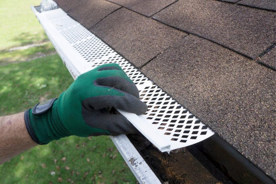 A green gloved-hand installs a gutter guard, as seen from above. 