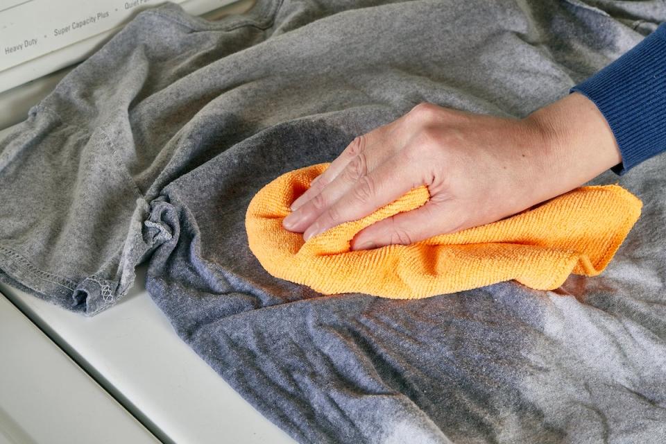 Woman uses orange cloth to blot a wet shirt.