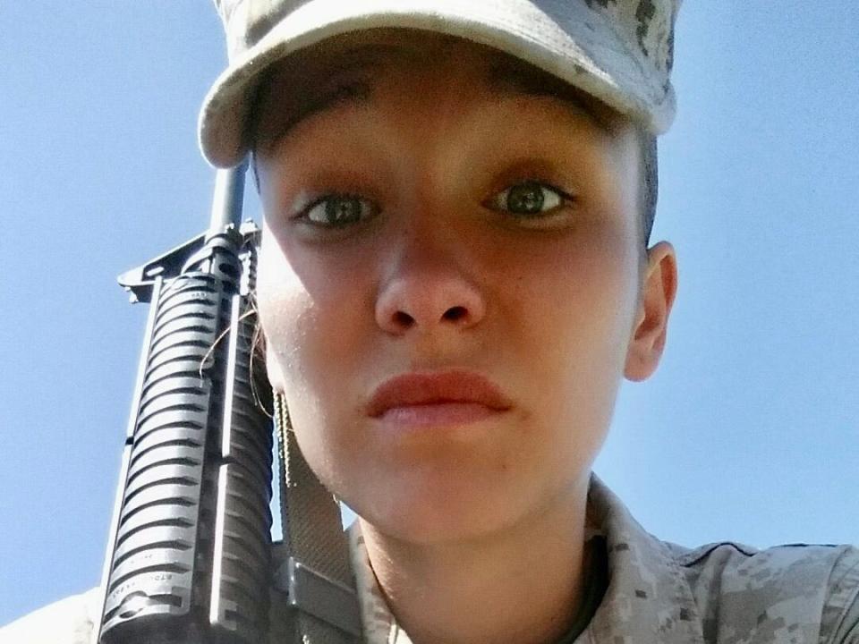 A female marine looking into the camera with a gun on her shoulder.