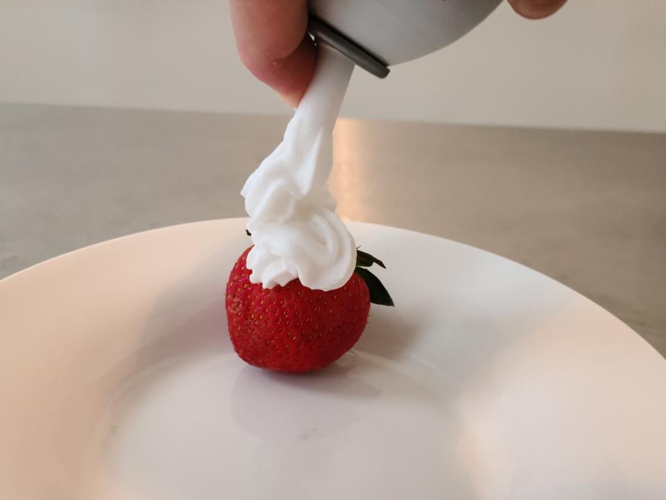 hand spraying coconut whipped cream onto a strawberry