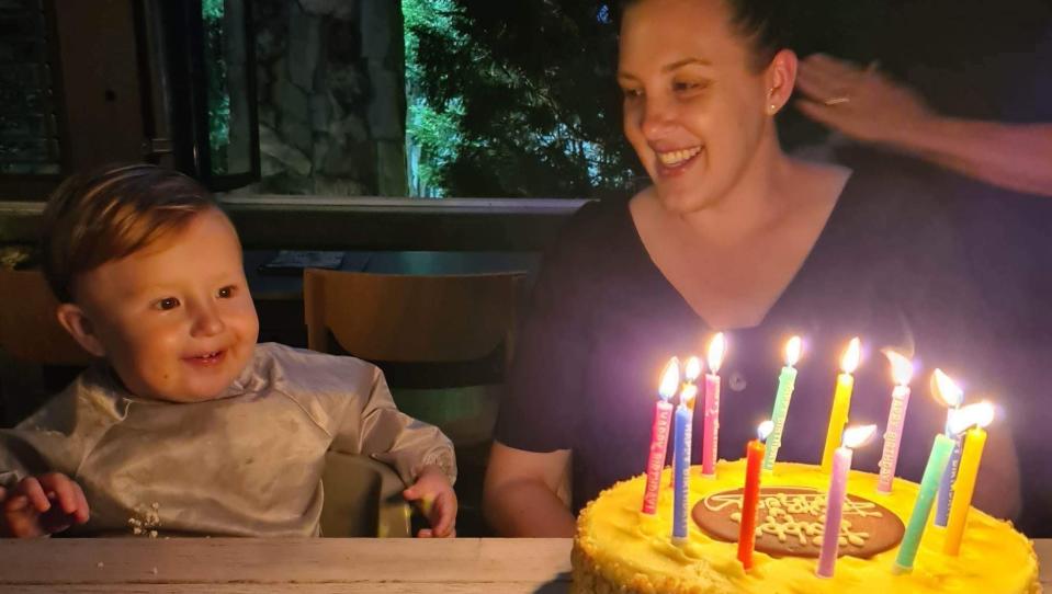 Amy smiling at her son Nicholas as he looks at a yellow birthday cake with candles. 