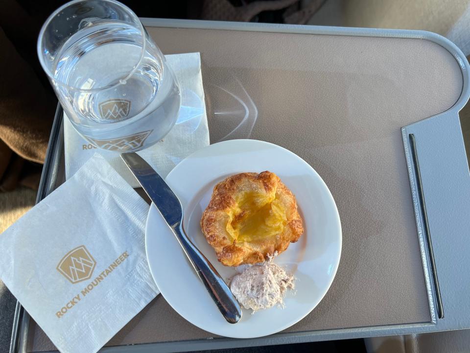A train car tray with a glass of water, a napkin, and a pastry on a plate