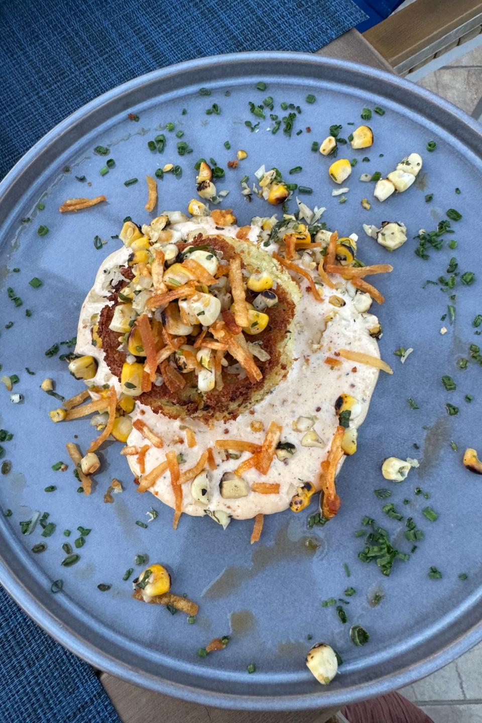 A plate with a fried item topped with sauce and sprinkled with shredded vegetables and corn, presented on a table