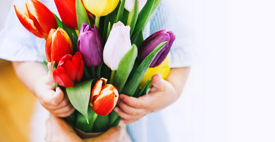 Beautiful tulips in child hands. Cute little girl with flowers bouquet for Mother's Day, Easter and Spring background