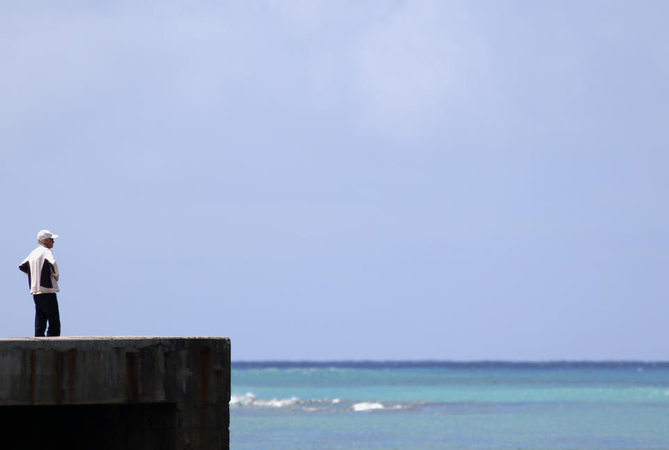 A man stands on a closed pier on Waikiki Beach in Honolulu on Saturday, March 28, 2020. Like many cities across the world, Honolulu came to an eerie standstill this weekend as the coronavirus pandemic spread throughout the islands. But Hawaii officials went beyond the standard stay-at-home orders and effectively flipped the switch on the state's tourism-fueled economic engine in a bid to slow the spread of the virus. As of Thursday, anyone arriving in Hawaii must undergo a mandatory 14-day self-quarantine. The unprecedented move dramatically reduced the number of people on beaches, in city parks and on country roads where many people rely on tourism to pay for the high cost of living in Hawaii. (AP Photo/Caleb Jones)