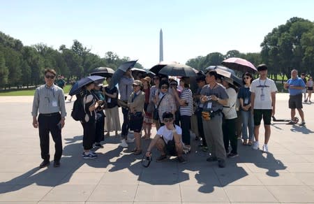 Tourists huddle under umbrellas to protect themselves against the sun in the plaza in front of the Lincoln Memorial with the Washington Monument in the background, on a day when the temperature was forecast to reach 99 degrees F, in Washington