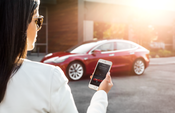 A woman unlocks her Model 3 with a Tesla app on her smartphone