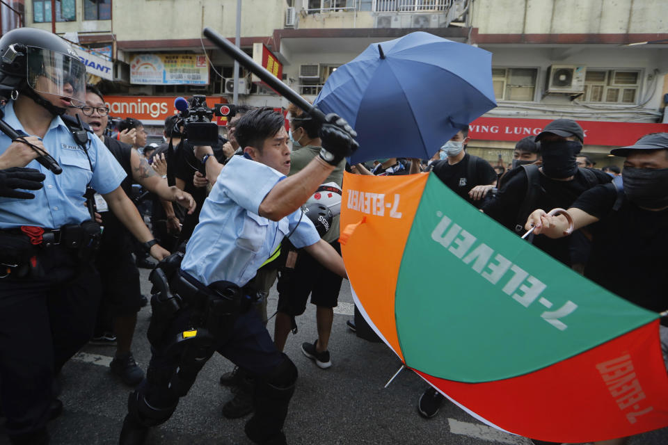 A police officer attacks protesters holding up umbrellas in Hong Kong Saturday, July 13, 2019. Several thousand people marched in Hong Kong on Saturday against traders from mainland China in what is fast becoming a summer of unrest in the semi-autonomous Chinese territory. (AP Photo/Kin Cheung)
