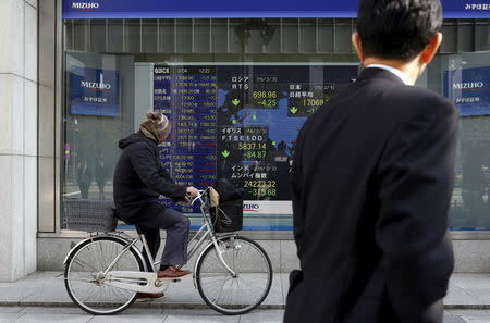 A man riding on a bicycle looks at an electronic board showing the stock market indices of various countries outside a brokerage in Tokyo, Japan, February 4, 2016. REUTERS/Yuya Shino
