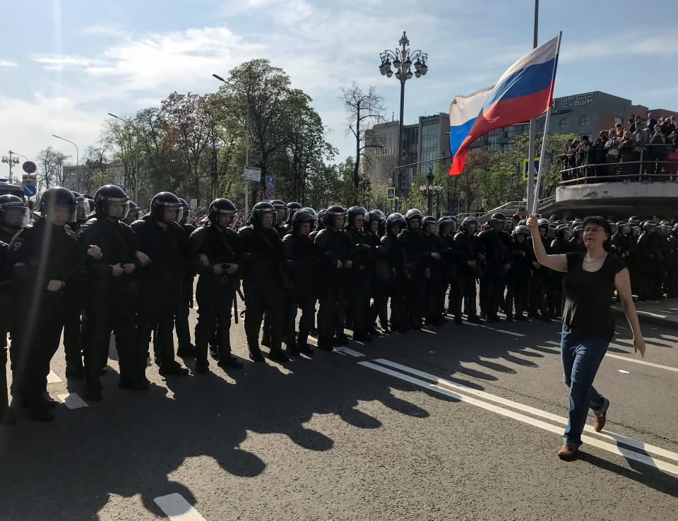 An opposition supporter carries a Russian national flag in front of police officers blocking a street during a protest rally ahead of President Vladimir Putin's inauguration ceremony, in Moscow, Russia May 5, 2018. REUTERS/Maria Tsvetkova