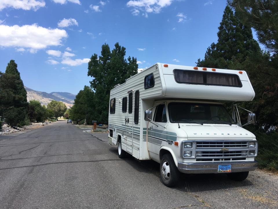 Large white RV parked on the side of the road with trees and blue skies in the background