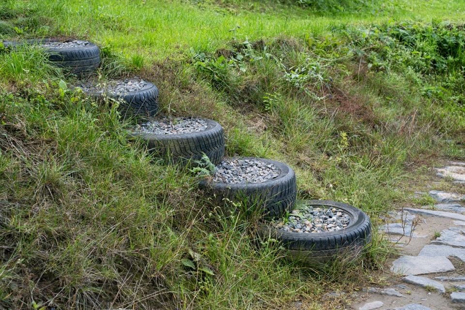 Old used car tires filled with granite rock stones to make stairs on on the slope in backyard. 