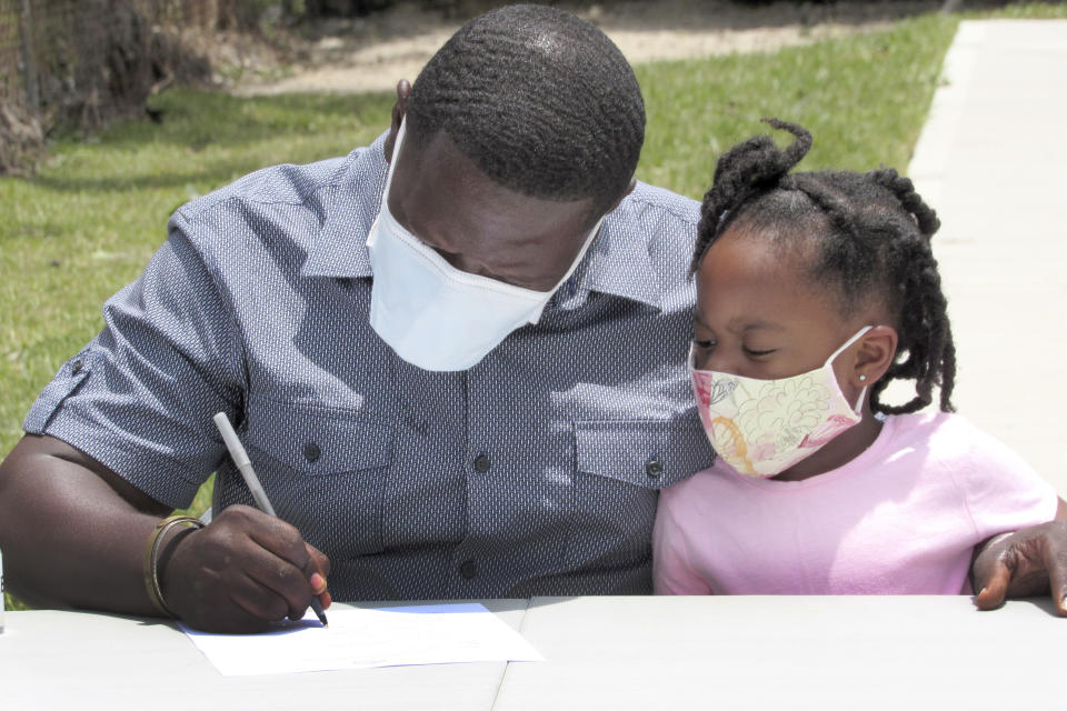 In this photo taken Friday, May 29, 2020, Houston resident Lloyd Nelms sits next to his niece as he signs paperwork before receiving the keys to his new house. Nelms' family home had to be torn down after it was flooded during Hurricane Harvey in 2017. Nelms said he was unable to get help from a city program created to fix homes damaged during Harvey and had to endure hazardous living conditions for more than two years. He turned to the Texas General Land Office to rebuild his home. The city program has finished rebuilding less than 70 homes since beginning in January 2019. (AP Photo/Juan Lozano)