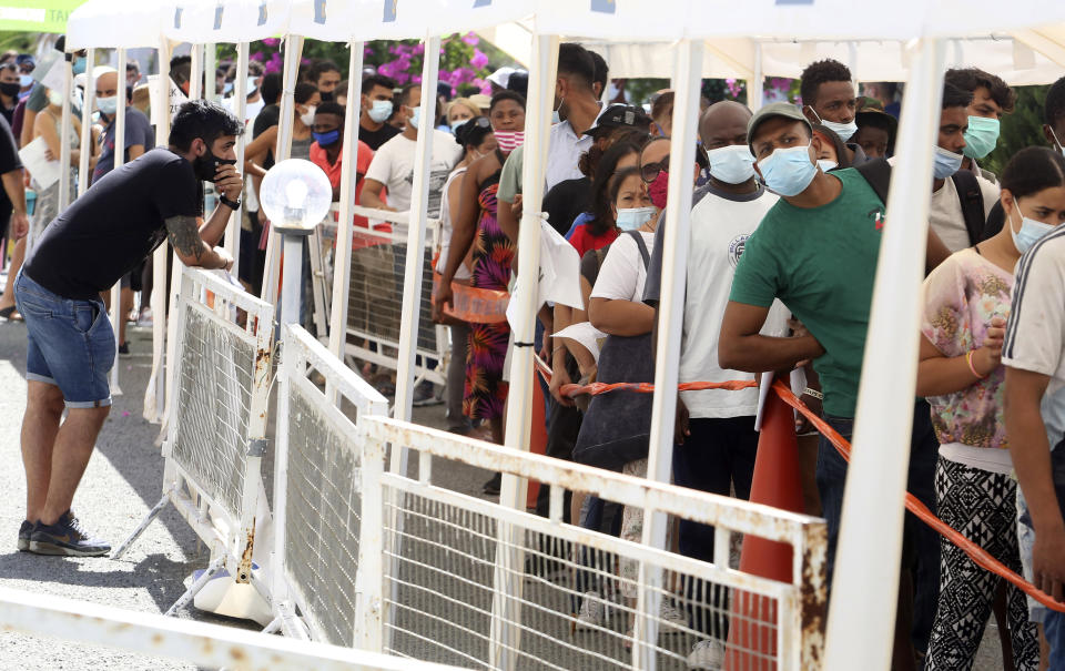 People wait in line to receive a vaccine shot against COVID-19 at a 'Walk-in' vaccination center on the grounds of Cyprus' State Fair in the capital Nicosia, Cyprus, on Friday, Aug. 13, 2021. Cypriot authorities have been surprised by the huge turnout since the center last week began offering without an appointment, free of charge shots to those who aren't covered under the country's national health scheme.(AP Photo/Philippos Christou)