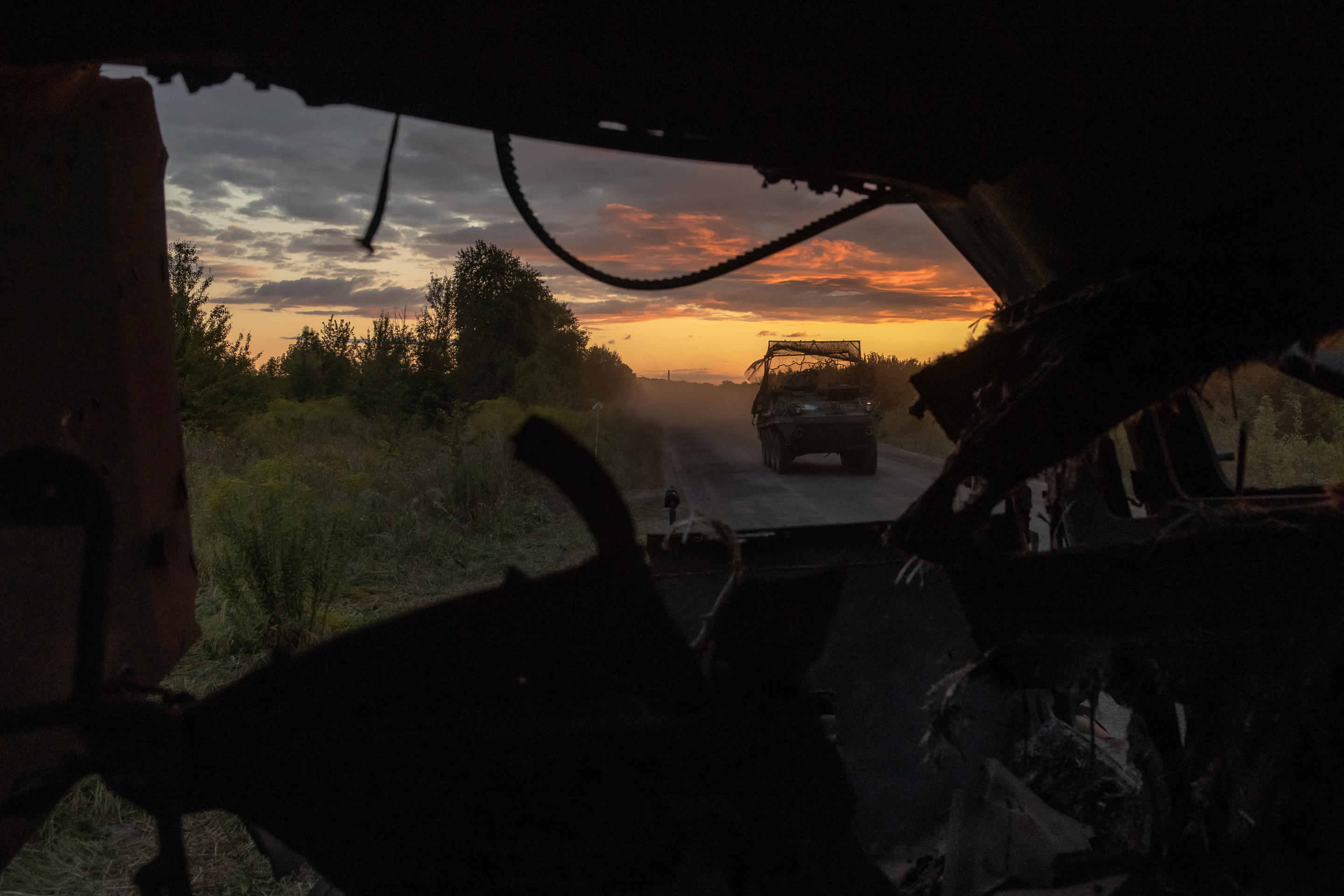 A military vehicle drives past a destroyed Ukrainian military vehicle. 