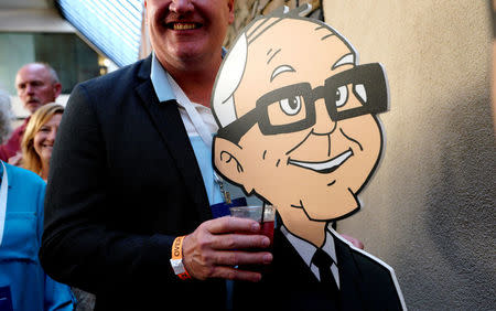 A shareholder holds a drink posing with a cartoon Warren Buffett at the opening cocktail party for the Berkshire Hathaway Inc annual meeting, the largest in corporate America, in its hometown of Omaha, Nebraska U.S. May 4, 2018. REUTERS/Rick Wilking