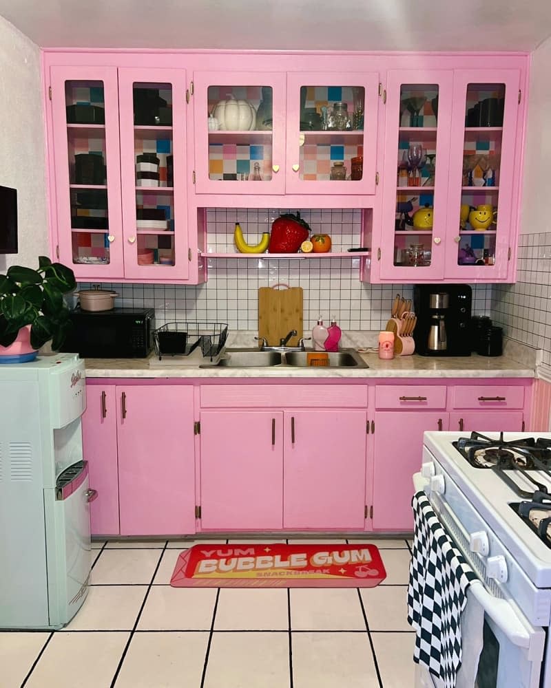 Kitchen with pink cabinets, marble countertop, white tile backsplash and flooring, and water cooler.