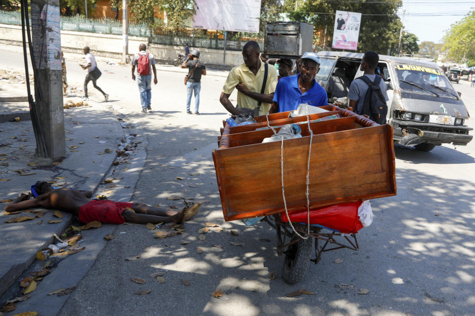 A man pushes a cart past the body of a man shot by unidentified assailants in downtown Port-au-Prince, Haiti, Monday, March 4, 2024. (AP Photo/Odelyn Joseph)