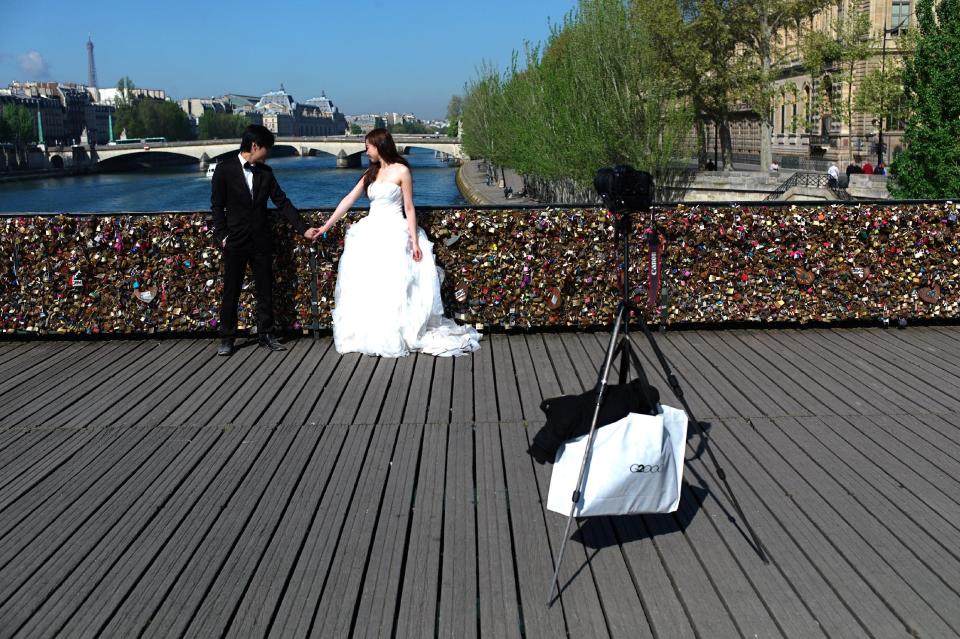 This April 9, 2014 photo shows a just married couple holding hands on the Pont des Arts in Paris. A recent fad among travelers of hitching padlocks on bridges and at tourist attractions worldwide to symbolically immortalize their amorous attraction has swept up this reputed City of Love more than most. Now, two American-born women who live in Paris say they've had enough, launching a petition drive to try to get mostly laissez-faire city officials to step in and do something about what they call an unbearable eyesore in a majestic municipality. (AP Photo/Thibault Camus)