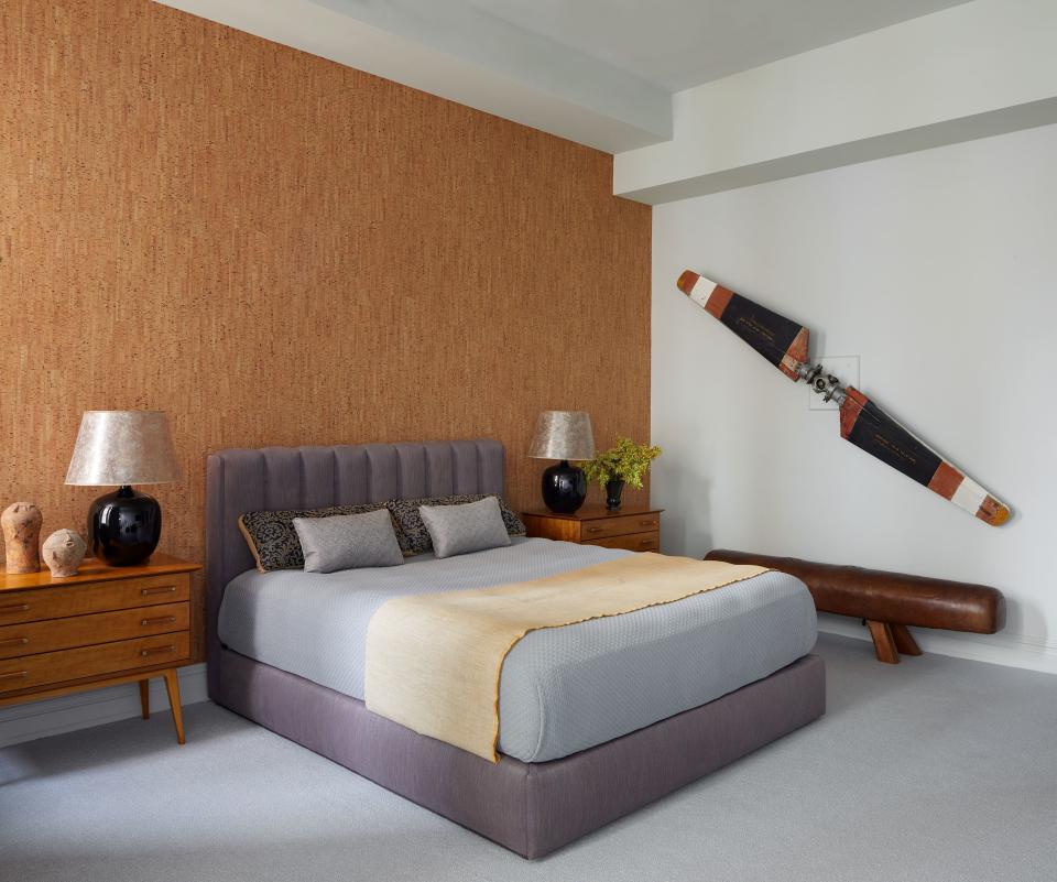 A cork wall covering establishes an earthy backdrop for a serene master bedroom. Huniford provided the vintage helicopter propeller blade and mica-hued lampshades.