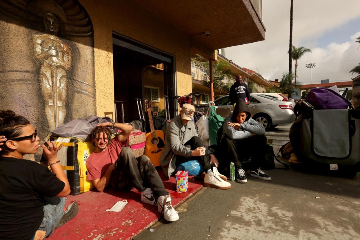 People sit on the ground outside a building with their belongings