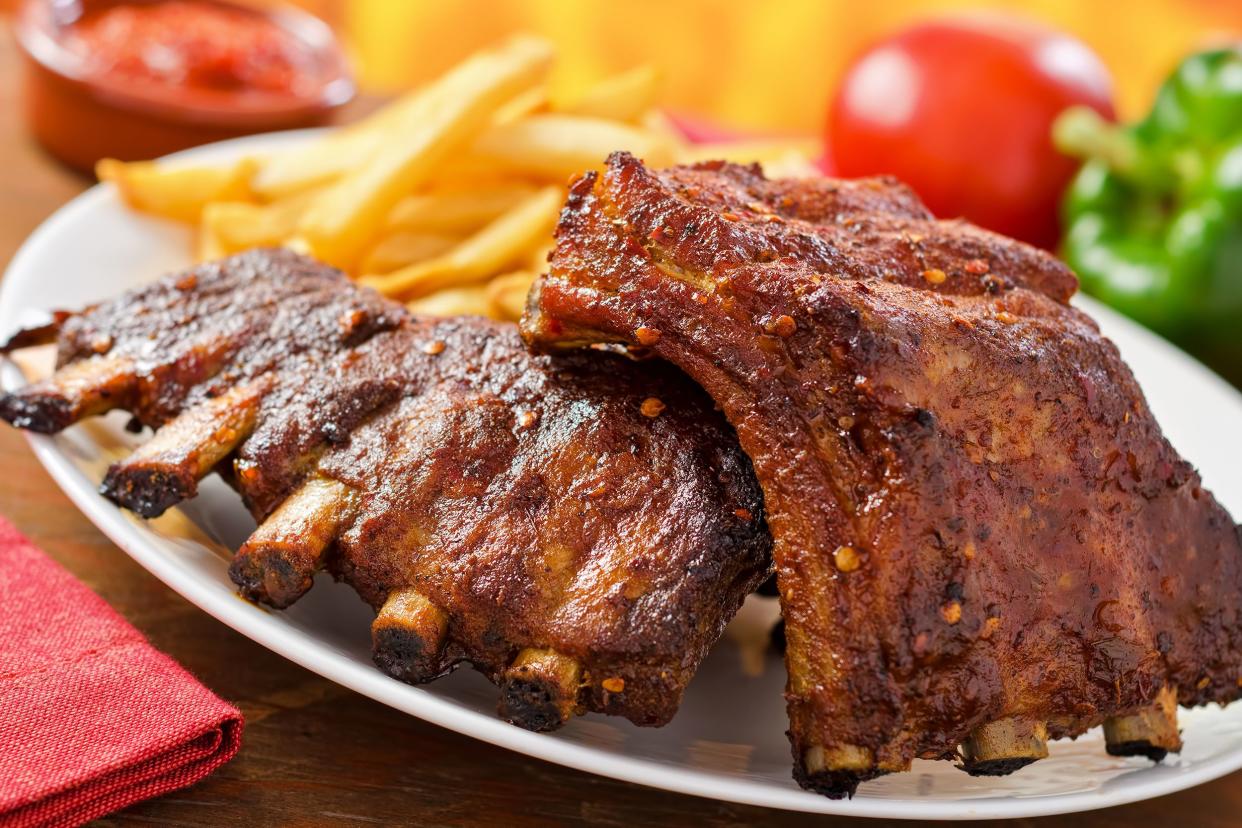 Great ribs in the oven on a white plate, selective focus, with French fries on the other side of the plate with ingredients blurred in the background