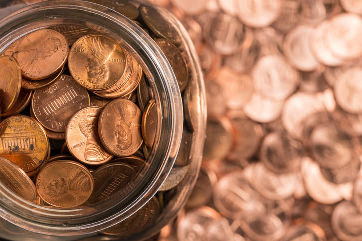 Open glass jar filled with US pennies, more scattered around it