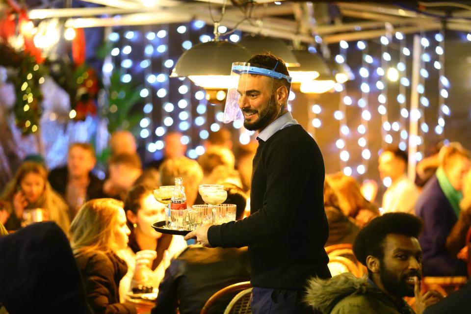 <p>A man serves drinks to an outdoor table in the West End in December before the capital was plunged into Tier 4</p> (PA)