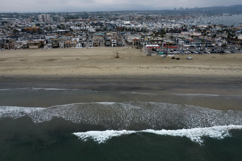 FILE - This aerial image taken with a drone, shows the closed beach after oil washed up in Newport Beach, Calif., on Oct. 7, 2021. A pipeline operator has agreed to pay $50 million to Southern California fishermen, tourism companies and property owners who sued over an offshore oil spill last year. A proposed settlement between Amplify Energy Corp. and the businesses was filed Monday Oct. 17, 2022, in federal court. (AP Photo/Ringo H.W. Chiu, File)