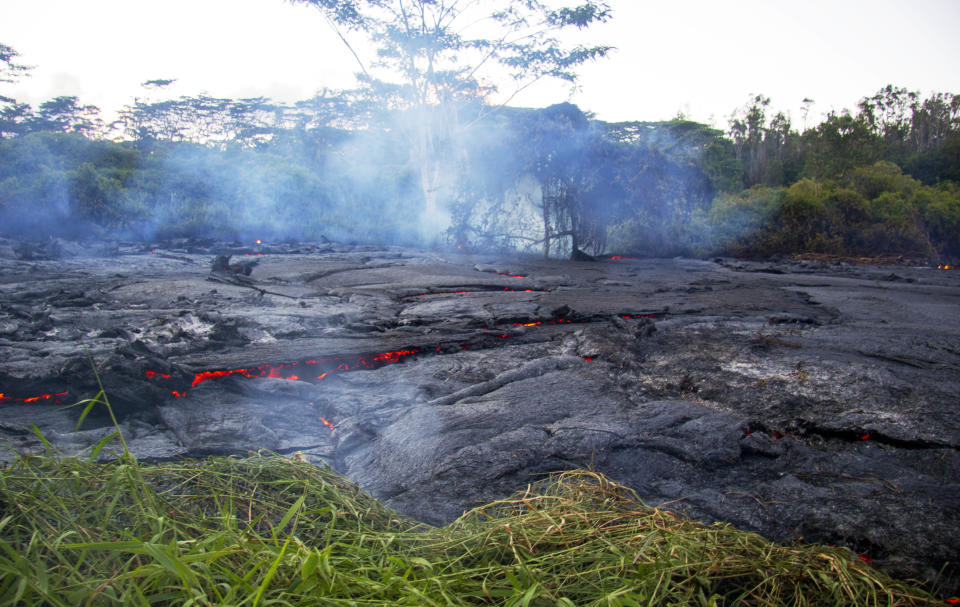 This Oct. 22, 2014 photo provided by the United States Geological Survey shows lava flow slowly moving through thick vegetation and creating thick plumes of smoke as it advances on the town of Pahoa on the Big Island of Hawaii. Frequent methane explosions occur, resulting from cooked vegetation releasing methane which then ignites. The explosions can range from small puffs to loud cannon-like blasts, and are an additional hazard in the immediate area of the flow margin. (AP Photo/U.S. Geological Survey)