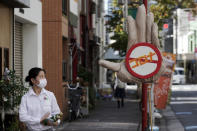 A woman wearing a protective mask to help curb the spread of the coronavirus walks past a scarecrow depicting a big hand with stop coronavirus sign displayed at a street Monday, Sept. 28, 2020, in Tokyo. The Japanese capital confirmed more than 70 coronavirus cases on Monday. (AP Photo/Eugene Hoshiko)