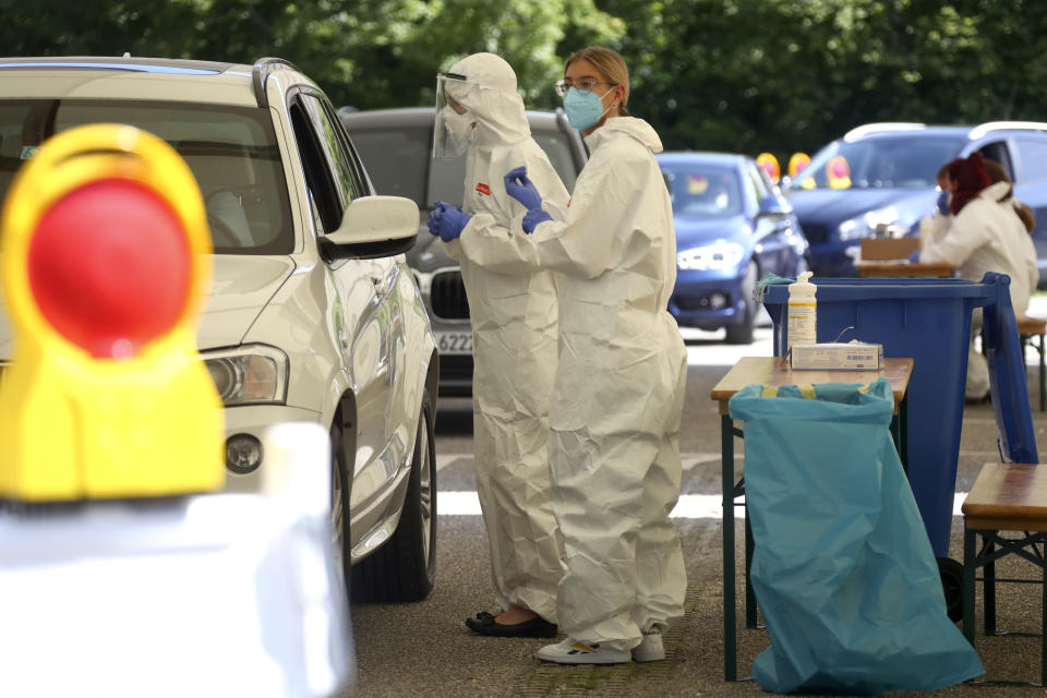 Health workers collect samples at a makeshift COVID-19 testing station in Mamming, Germany, Tuesday July 28, 2020. After a local coronavirus outbreak on the cucumber farm premises, state authorities have quarantined the entire farm and its workers. (AP Photo/Matthias Schrader)