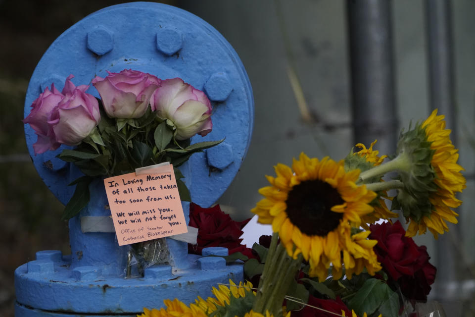 Flower bouquets are left in memory of the shooting victims on top of a water pipe as law enforcement personnel stage at the scene of a mass shooting at Cook's Corner, Thursday, Aug. 24, 2023, in Trabuco Canyon, Calif. (AP Photo/Damian Dovarganes)