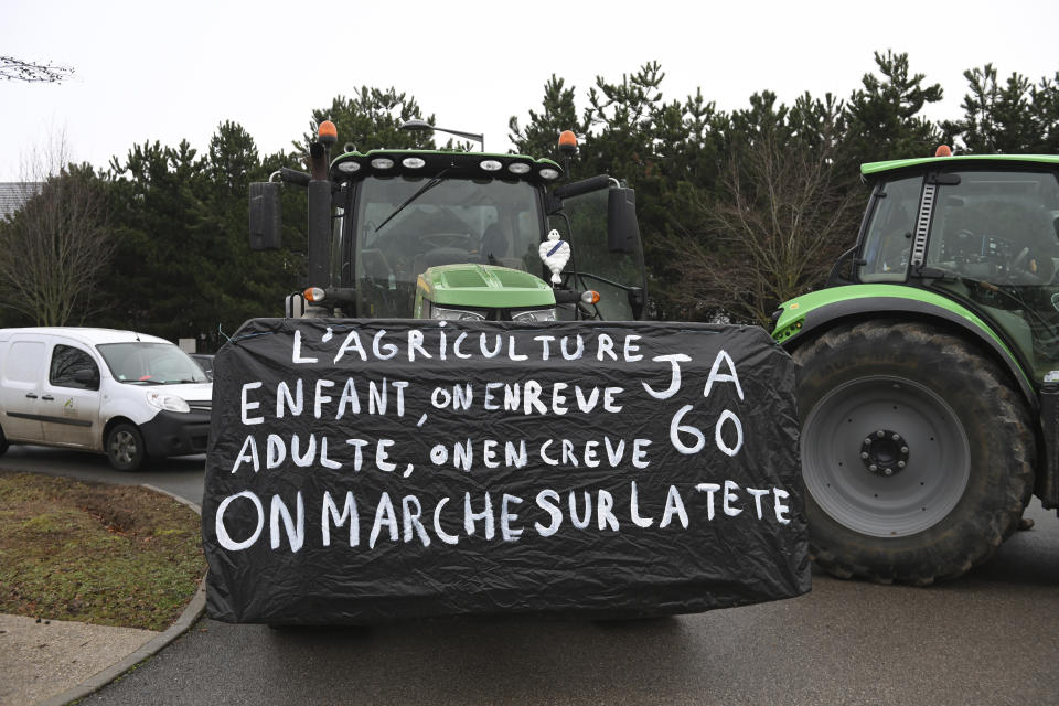 Farmers gather before a demonstration Tuesday, Jan. 23, 2024 near Beauvais, northern France. Farmers have for months been protesting for better pay and against what they consider to be excessive regulation, mounting costs and other problems. Banner reads: farming, a childhood dream that kills us as adults,. The world is upside down. (AP Photo/Matthieu Mirville)