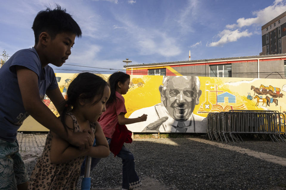 Children run past a mural featuring Pope Francis outside Saints Peter and Paul Catholic Cathedral in Ulaanbaatar, Mongolia on Thursday, Aug. 31, 2023. Pope Francis is travelling to Mongolia to encourage one of the world’s smallest and newest Catholic communities. It's the first time a pope has visited the Asian country. (AP Photo/Louise Delmotte)