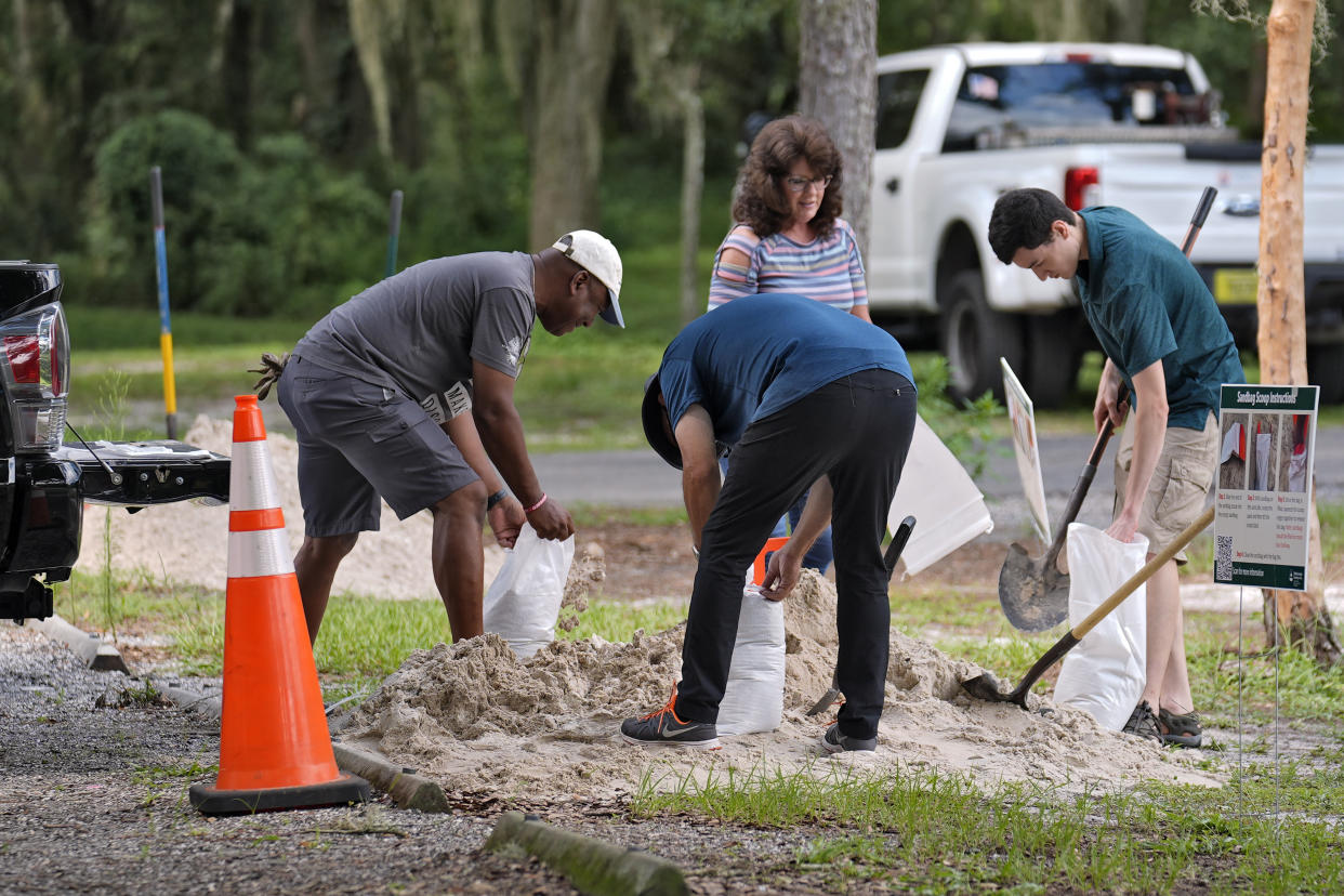 Four people use shovels to fill sandbags.