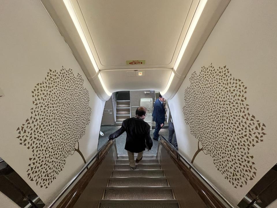 Looking down the front staircase onboard an Emirates A380, with ornate gold tree designs on the white wallpaper