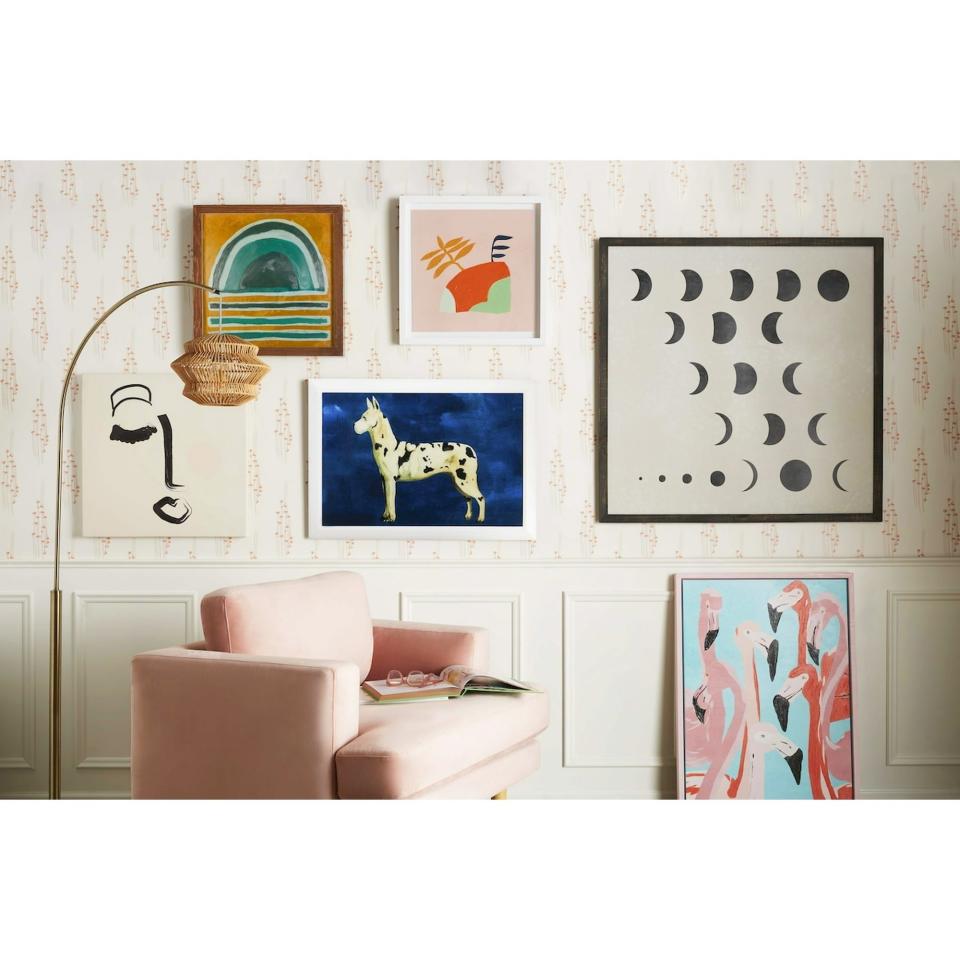 A stylish living room wall with various art pieces and a pink chair. Art includes a rainbow, horse, lunar phases, abstract faces, and colorful flamingos