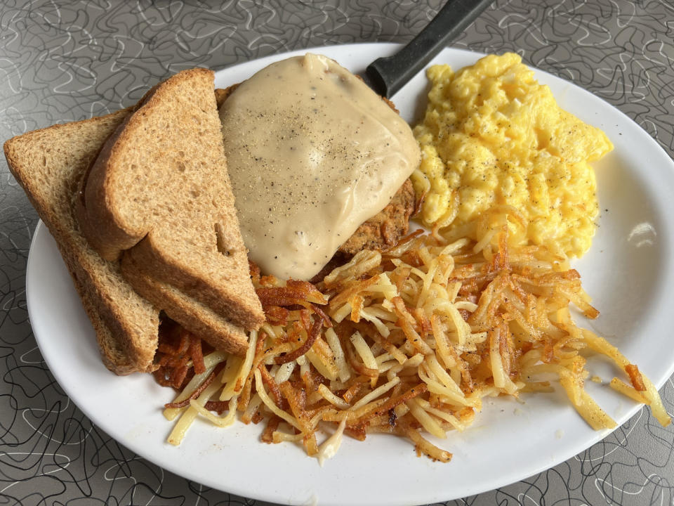 A plate with toast, scrambled eggs, hash browns, and a breaded patty topped with gravy